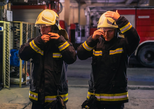 Porträt zweier junger Feuerwehrmänner in Uniform, die in der Tanne stehen - Foto, Bild