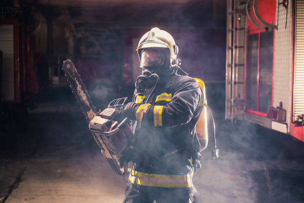 Portret van een jonge brandweerman die een kettingzaag in de - Foto, afbeelding