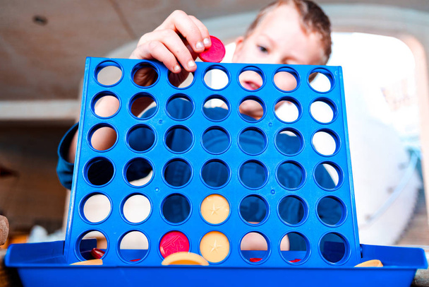 Dziecko gra w tradycyjną grę strategiczną, aby utworzyć 4 wiersz żetonów. - Zdjęcie, obraz