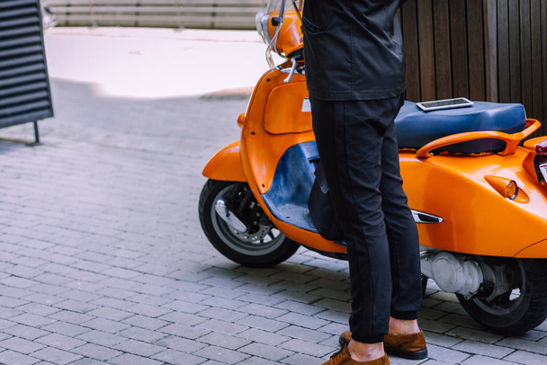 Zwyczajny miejski profesjonalny biznesmen stojący w pobliżu pomarańczowego motocykla vespa - Zdjęcie, obraz