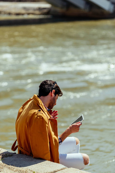 Νεαρός πληκτρολογώντας μήνυμα στο tablet του και απολαμβάνοντας την ηλιόλουστη μέρα - Φωτογραφία, εικόνα