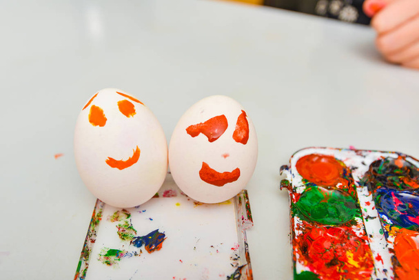 Δύο αυγά με ζωγραφισμένο πρόσωπο κείτονται δίπλα στις ακουαρέλες μετά την τέχνη. - Φωτογραφία, εικόνα