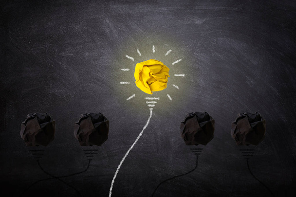 Business Idea Concept : Yellow crumpled paper ball light bulb lighting grow around on chalkboard. - Photo, Image