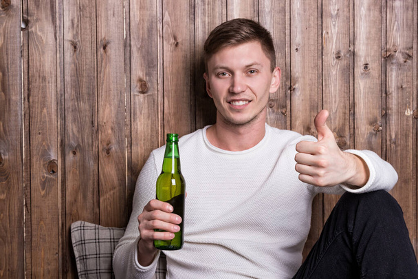 Young handsome man sitting near wood wall and drinking beer - Zdjęcie, obraz