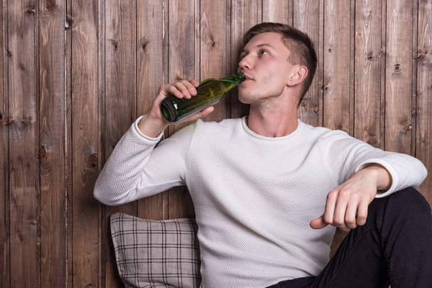 Jovem homem bonito sentado perto da parede de madeira e beber cerveja
 - Foto, Imagem