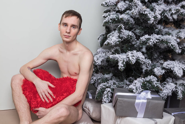 Young man with big present sitting on floor near christmas tree - Foto, imagen