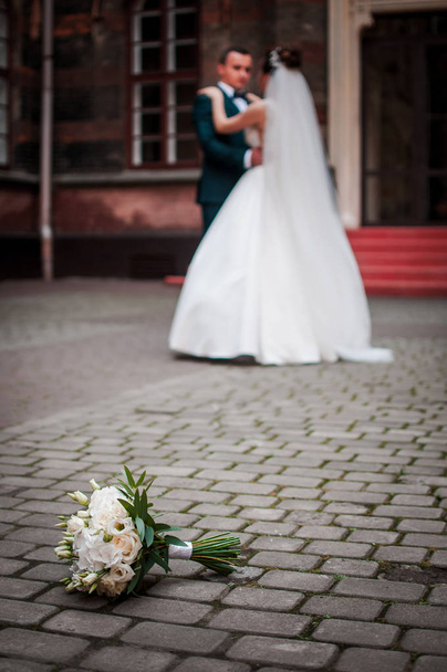 Páros vőlegény és menyasszony a hátsó fókusz és csokor virág fekszik a járdán - Fotó, kép