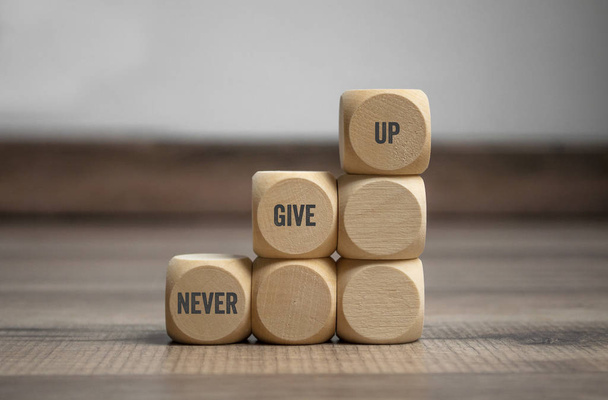 Pyramide made of cubes and dice with message Never give up on wooden background - Photo, Image