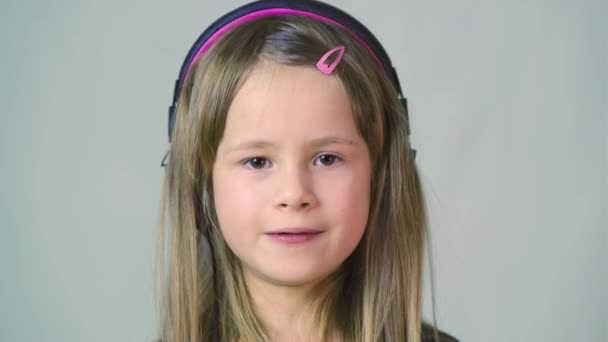 Jolie fille cild souriante écoutant de la musique dans de gros écouteurs roses
. - Séquence, vidéo