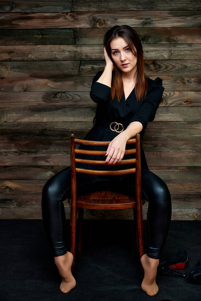 The concept of a glamorous portrait. Portrait of a pretty brunette girl in a black fashion suit on a stylish background in the original interior. Sits on a chair in various poses. - Photo, image