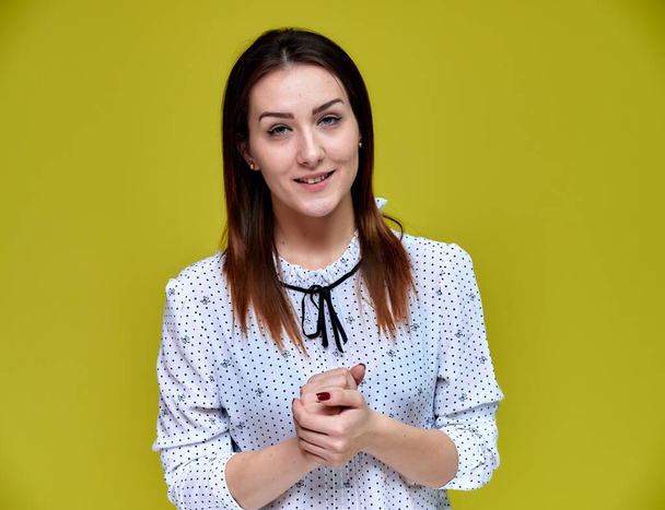The concept of an office worker, teacher, manager. Portrait of a pretty brunette girl in a white business blouse smiling, talking to the camera on a yellow background. - Photo, Image