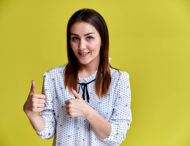 The concept of an office worker, teacher, manager. Portrait of a pretty brunette girl in a white business blouse smiling, talking to the camera on a yellow background. - Foto, imagen
