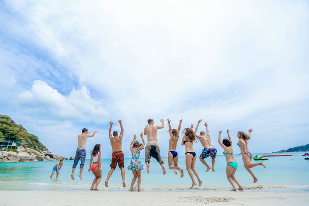 La compañía de amigos saltan todos juntos en el océano con las manos en alto
 - Foto, imagen