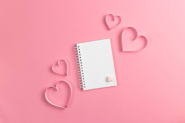Composition for Valentines Day February 14th. Delicate pink background and notebook with recognition. A heart cut out of paper. Greeting card. Flat lay, top view, copy space. - 写真・画像