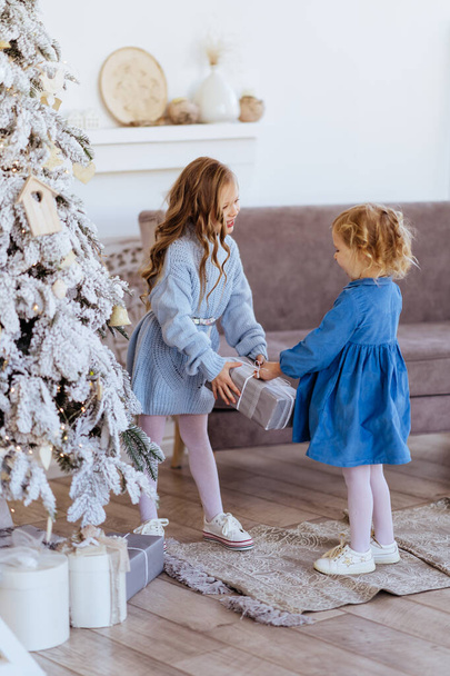 Two cute adorable little sisters near christmas tree in cozy living room. - Photo, image