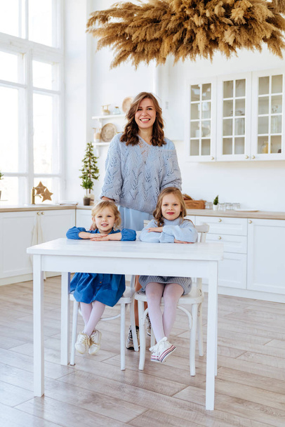 Mom with her two children sitting on the kitchen table. - Valokuva, kuva
