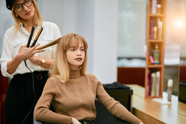 professional hair stylist make hairdo to young caucasian girl - Fotó, kép