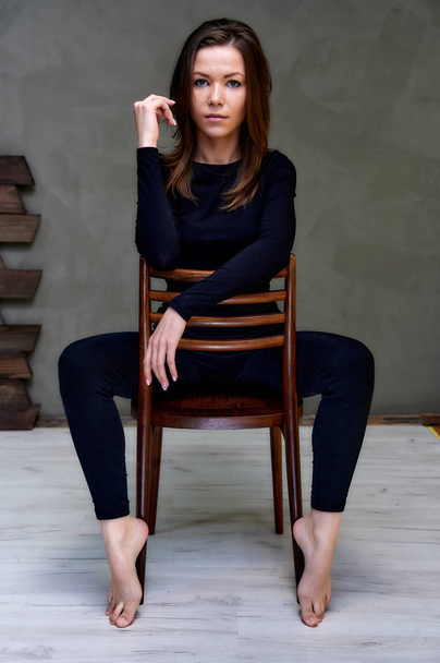 Vertical Photo on a chair in a stylish interior in a studio of a pretty glamorous brunette. girl sitting on a chair in a black T-shirt with long hair on a color fashionable original background. - Foto, imagen