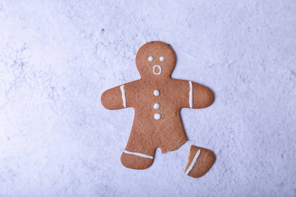 Gingerbread man with a broken leg (without leg) and with a surprised face. Traditional New Year and Christmas homemade cookies. Selective focus, close up. - Zdjęcie, obraz