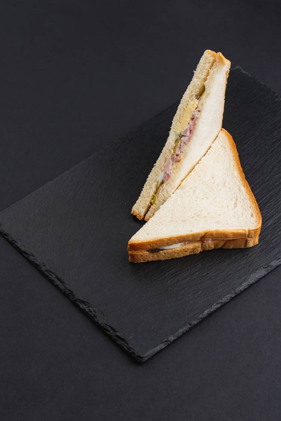 Pane bianco triangolare con pancetta, formaggio e uova sulla tavola nera  - Foto, immagini