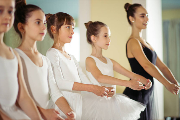 attractive slim ballerina in black tutu skirt show right poses in ballet to kids - Fotoğraf, Görsel