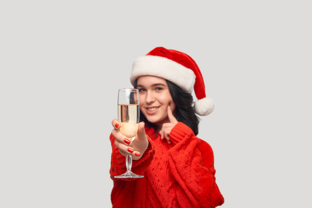Hermosa chica morena en un suéter rojo y Santa sombrero sosteniendo una copa de champán
. - Foto, imagen