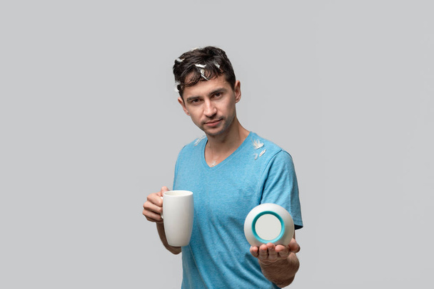 junger brünetter Mann mit weißer Tasse und Wecker isoliert über grauem Hintergrund. - Foto, Bild