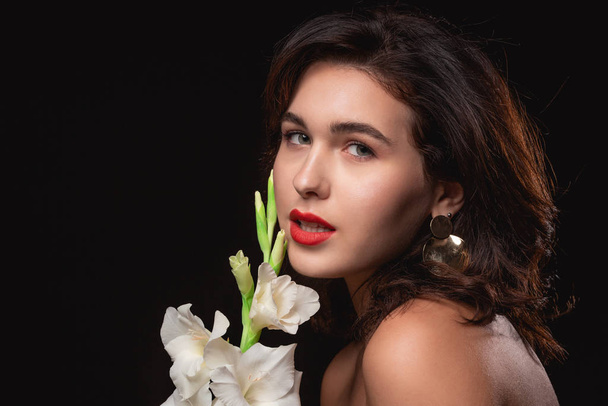 schöne Frau mit hellem Make-up posiert isoliert über schwarzem Hintergrund mit weißer Blume. - Foto, Bild