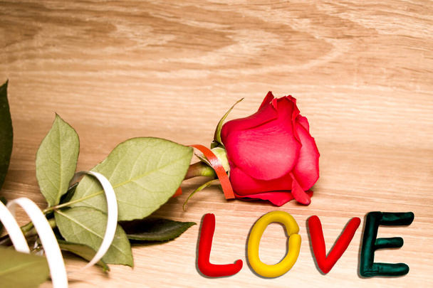 Όμορφο εορταστικό τριαντάφυλλο και η λέξη αγάπη. Σε ξύλινο φόντο. Ημέρα του Αγίου Βαλεντίνου. Έννοια σχεδιασμού. - Φωτογραφία, εικόνα