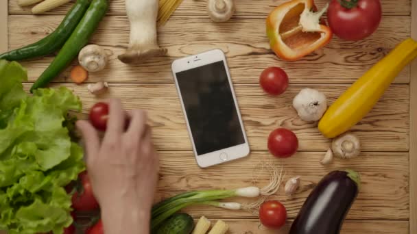 Males hand taking smartphone from table with vegetables - Footage, Video