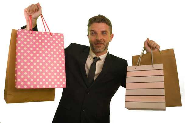 isolated background portrait of young attractive and happy business man in suit and tie holding lot of shopping bags smiling cheerful in sales and opportunity concept  - Foto, imagen