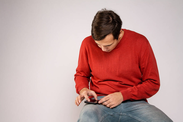 The guy in the red sweater is using a smartphone. Examines the image - Φωτογραφία, εικόνα