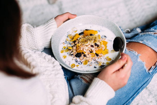 White cat eats muesli with banana and chia seeds from a plate in a girl's hands - Valokuva, kuva