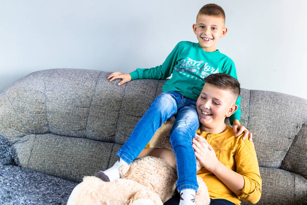 Two brothers sitting on couch in living room, watching television together - Zdjęcie, obraz