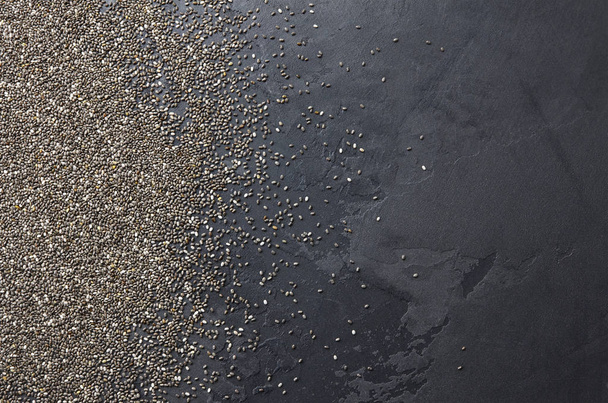Raw organic chia seeds over black stone texture background, top view, copy space - Valokuva, kuva