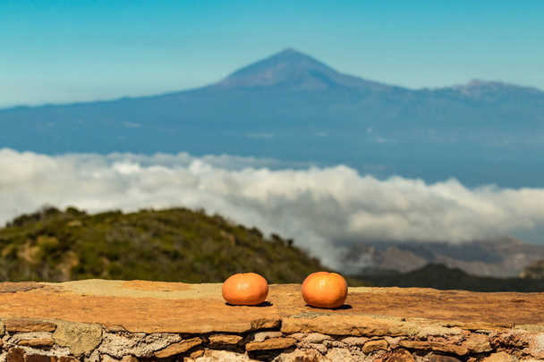 Close up, selective focus. Tangerines on a stone parapet. On a blurred background - a fantastic view of Tenerife flying in the clouds. Shot with a telephoto lens from the mountain peaks of La Gomera - 写真・画像