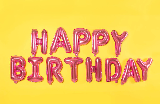Phrase HAPPY BIRTHDAY made of pink foil balloon letters on yellow background - Foto, Bild