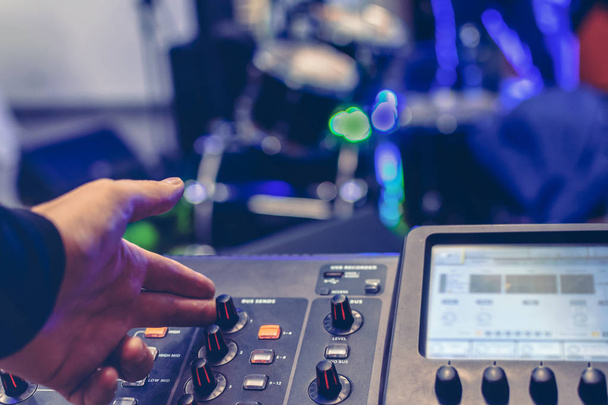 sound engineer hand adjusts sound on a modern digital console. drum set on stage blurred in the background - Photo, Image
