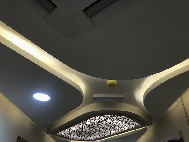 Un tablero decorativo de yeso suspendido falso techo con calas para la iluminación indirecta para una gran sala de área de un hospital especializado edificios interiores obra arquitectónica
 - Foto, imagen