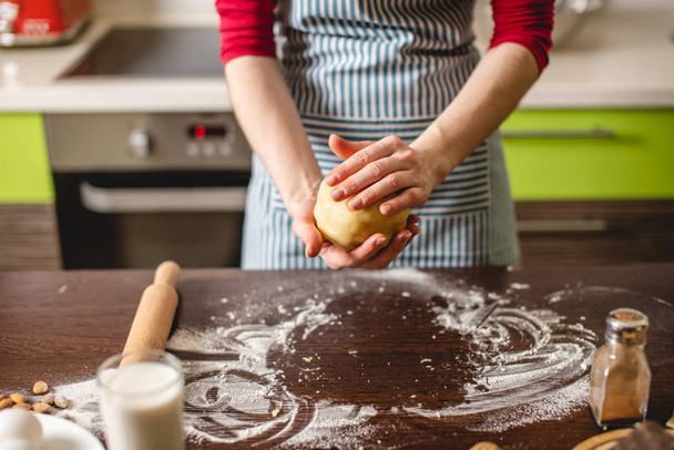 Cook νοικοκυρά κάνει μπισκότα στο σπίτι σε πολύχρωμη κουζίνα. Γυναίκα ζυμώνει τα χέρια ζύμης στο τραπέζι με συστατικά - Φωτογραφία, εικόνα