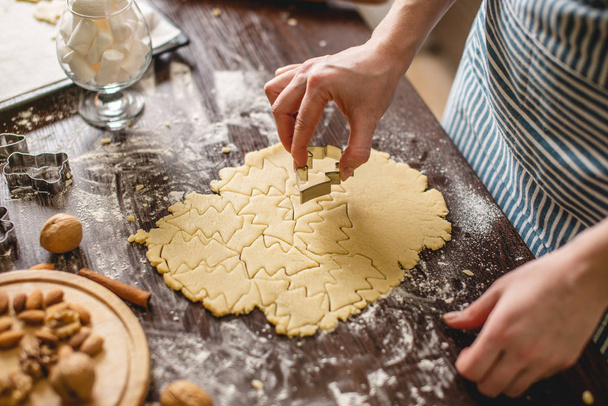 Cook νοικοκυρά κάνει χριστουγεννιάτικα μπισκότα στο σπίτι σε μια πολύχρωμη κουζίνα. Χέρια που κάνουν τη ζύμη σε σχήμα χριστουγεννιάτικου δέντρου - Φωτογραφία, εικόνα