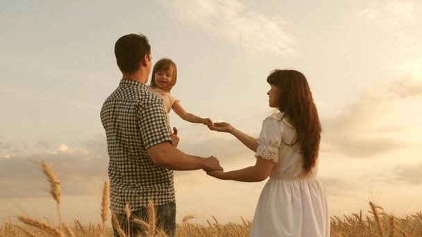 baby travels across field with her family. child and parent are playing. happy family and childhood concept. Happy baby in arms of father and mother. little daughter, dad and mom play in a wheat field - Фото, изображение