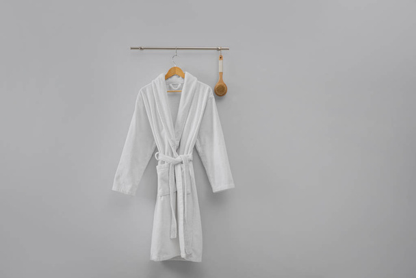 Hanger with clean bathrobe and brush on light wall. Space for text - Foto, Bild