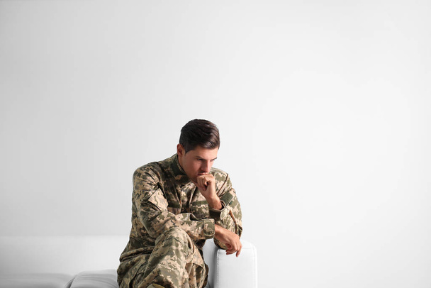 Stressed military officer sitting on sofa against white backgrou - Фото, изображение