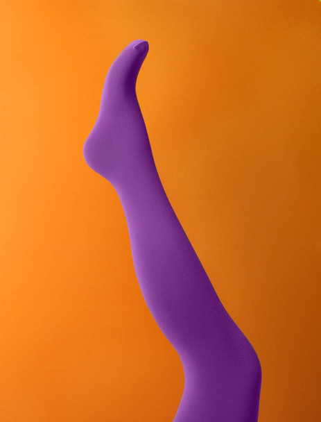 Leg mannequin in purple tights on orange background - Φωτογραφία, εικόνα