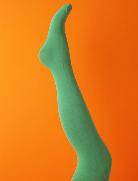 Leg mannequin in green tights on orange background - Фото, изображение