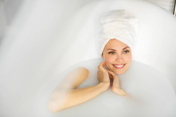 bela jovem com uma toalha na cabeça, encontra-se em um banho com leite
 - Foto, Imagem