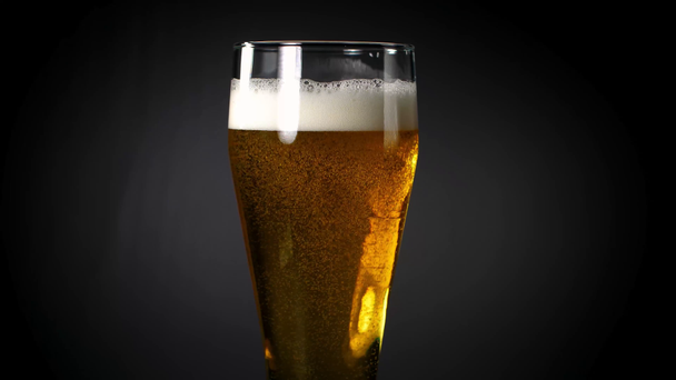 Beer poured into a glass on a black background - Felvétel, videó