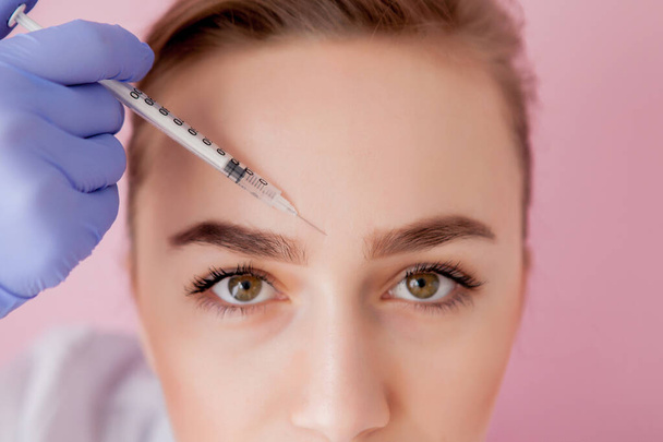El médico cosmetólogo realiza el procedimiento de inyecciones faciales rejuvenecedoras para apretar y alisar las arrugas en la piel de la cara de una hermosa mujer joven en un salón de belleza. - Foto, imagen