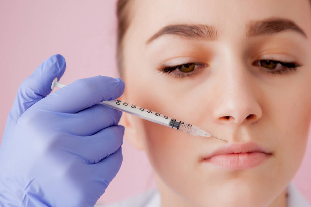 Doctor in gloves giving woman botox injections in lips, on pink background - Zdjęcie, obraz